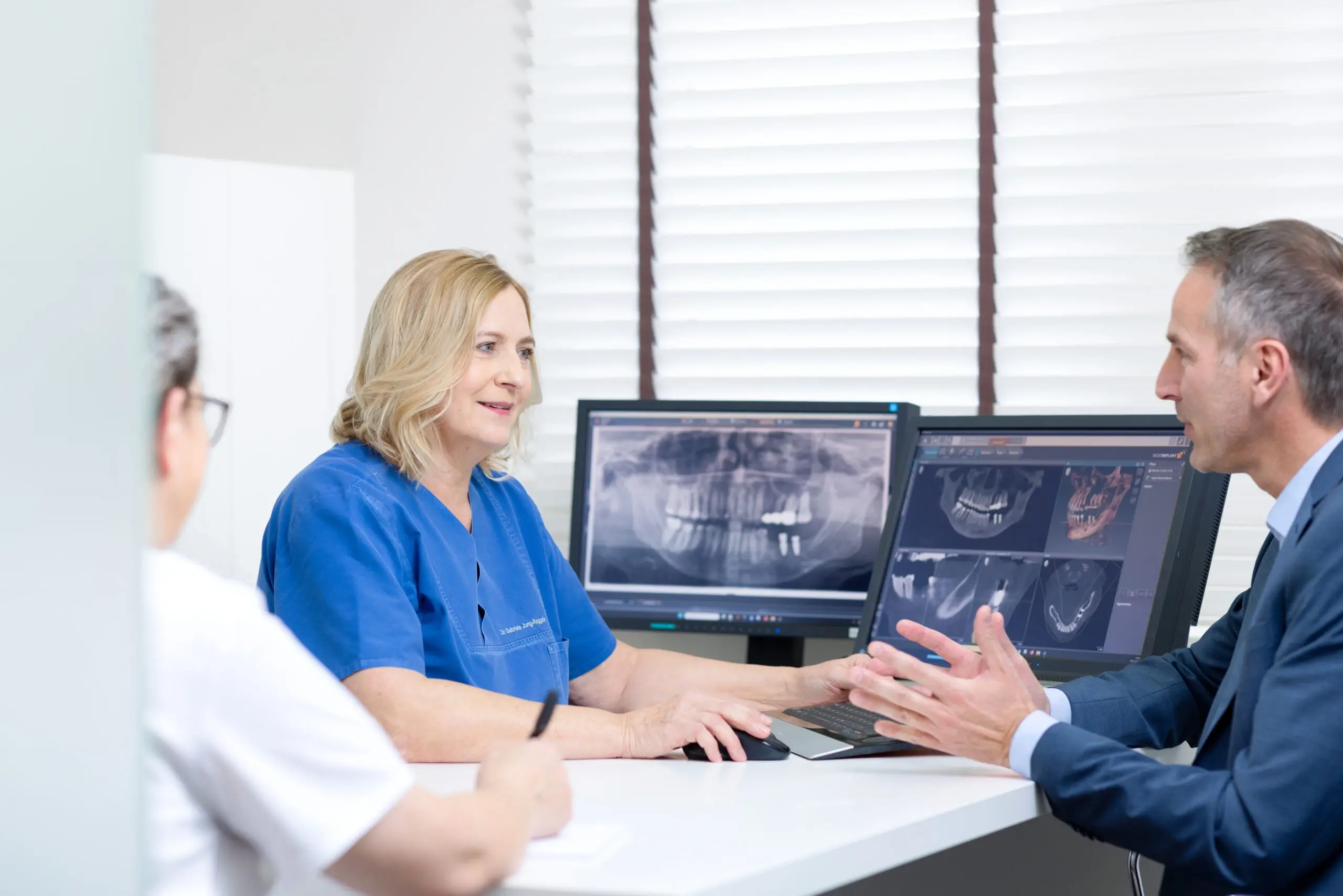 Zahnärztin und Zahnarzt zeigen einem Patienten die 3D-Planung